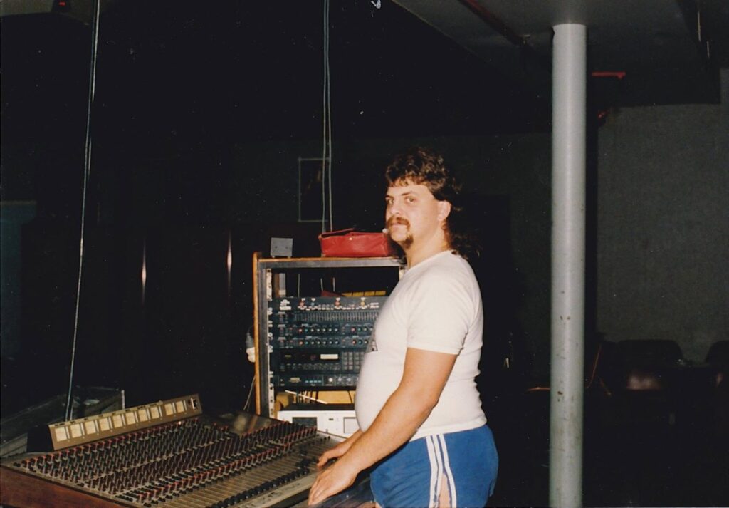 Mark Gibson at the mixing desk in a dark venue, with an effects rack behind him